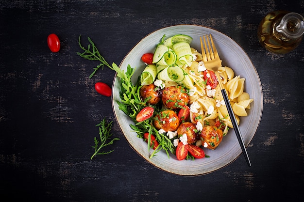 Italiaanse pasta. Conchiglie met gehaktballen, fetakaas en salade op donkere tafel. Diner. Bovenaanzicht, boven het hoofd. Slow food concept