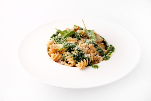 Italiaanse pasta met vlees kip plakjes kaas pesto en groene bladeren op brede witte plaat Bovenaanzicht op witte achtergrond