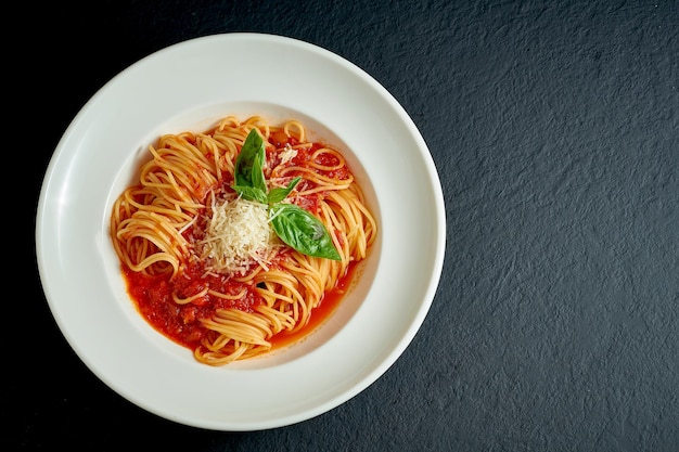 Italiaanse pasta spaghetti met tomaten en Parmezaanse kaas in een witte plaat op een donkere achtergrond