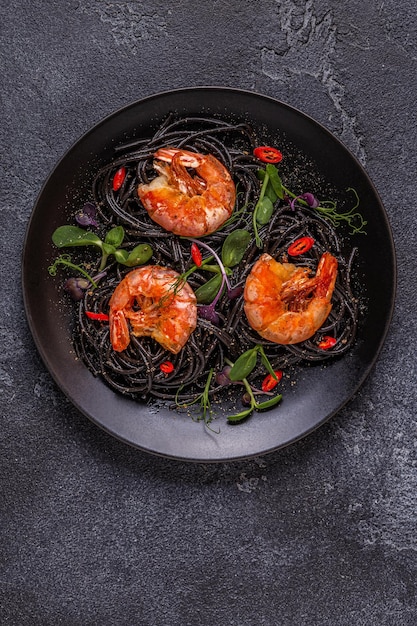 Italiaanse pasta zwarte spaghetti met garnalen en microgreens, bovenaanzicht.