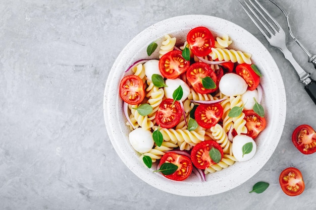 Italiaanse pastasalade met tomaten, mozzarella, kaas, rode ui en basilicum Bovenaanzicht kopieerruimte
