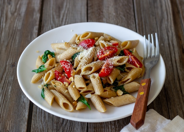 Italiaanse penne pasta met tomaten, spinazie, parmezaanse kaas, knoflook en noten. Gezond eten. Vegetarisch eten.