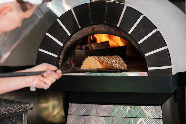 Foto italiaanse pizza houtkachel de kok voegt brandhout toe aan de kachel street food kookconcept
