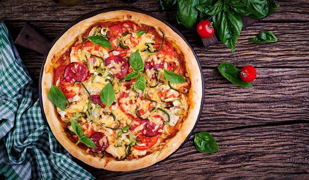 Italiaanse pizza met kip, salami, courgette, tomaten en kruiden op vintage houten tafel. . italiaanse keuken