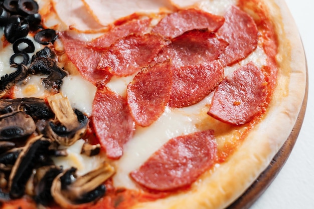 Italiaanse pizza met salami kaas, champignons en ham op een witte plaat vier soorten pizza in één close-up