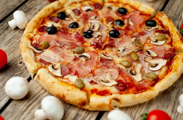 Italiaanse pizza met spek, champignons, olijven, tomaten op een houten achtergrond