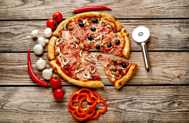 Italiaanse pizza met spek, champignons, olijven, tomaten op een houten achtergrond