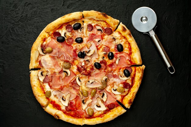 Italiaanse pizza met spek, champignons, olijven, tomaten op een zwarte betonnen achtergrond