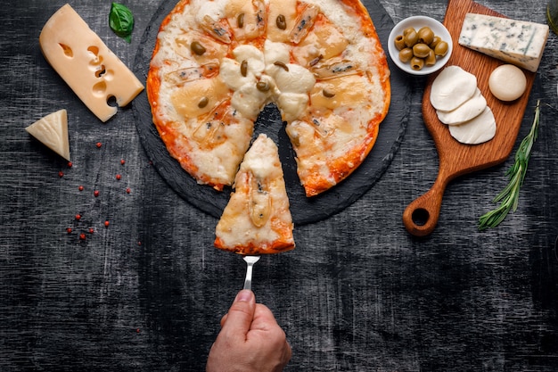 Italiaanse pizza met verschillende soorten kaas op een steen en een zwart gekrast bord.