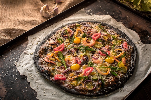 Italiaanse pizza met zwart deeg en zeevruchten op een bakplaat uit de oven. Daarop lagen inktvis, garnalen, octopus, uien, tomaten. inktvis inkt