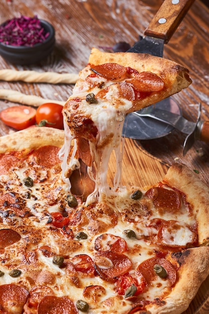 Foto italiaanse pizza op een houten tafel. een stuk hete pizza met kaas die zich uitstrekt.