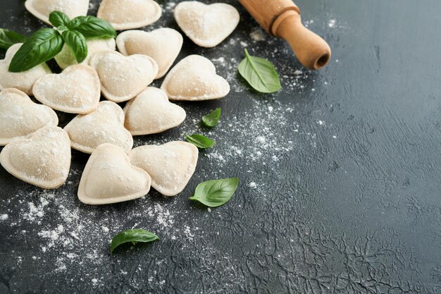 Italiaanse ravioli pasta in hartvorm Lekkere rauwe ravioli met bloem en basilicum op donkere achtergrond Voedsel koken ingrediënten achtergrond Valentijnsdag of Moederdag lunchideeën Top uitzicht met kopie ruimte