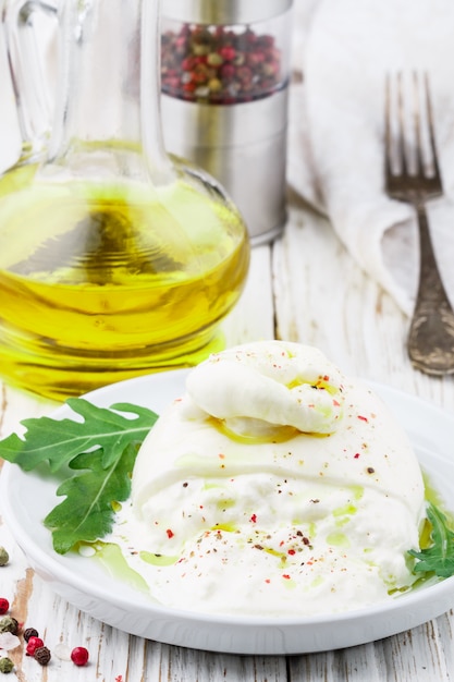 Italiaanse roomburratakaas met olijfolie, verse rucola, roze, groene en zwarte peper