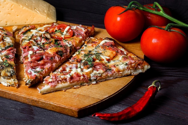 Italiaanse rustieke pizza drie stukken op een houten dienblad donkere houten tafel met tomaten, kaas en chili