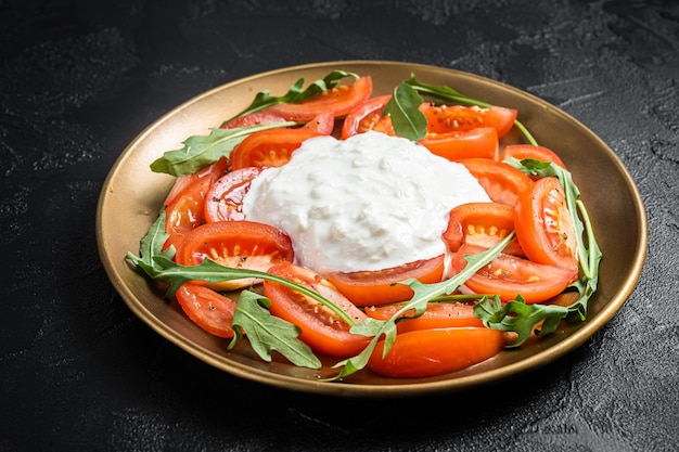 Italiaanse salade caprese met kaasstracciatella, tomaten en rucola. Zwarte achtergrond. Bovenaanzicht.