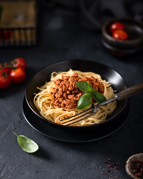 Italiaanse spaghetti bolognese in een zwarte kom, op tafel kerstomaatjes