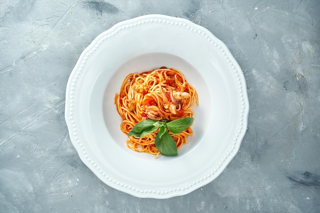 Italiaanse spaghetti pasta met tomaten en garnalen in een witte plaat op een grijze achtergrond