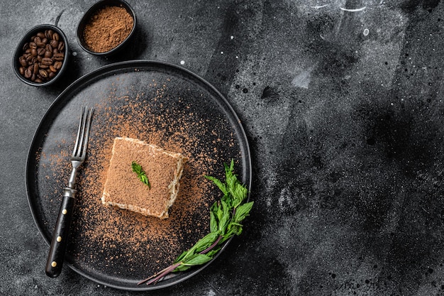 Italiaanse Tiramisu-cake met cacao en munt op een bord. Zwarte achtergrond. Bovenaanzicht. Ruimte kopiëren.