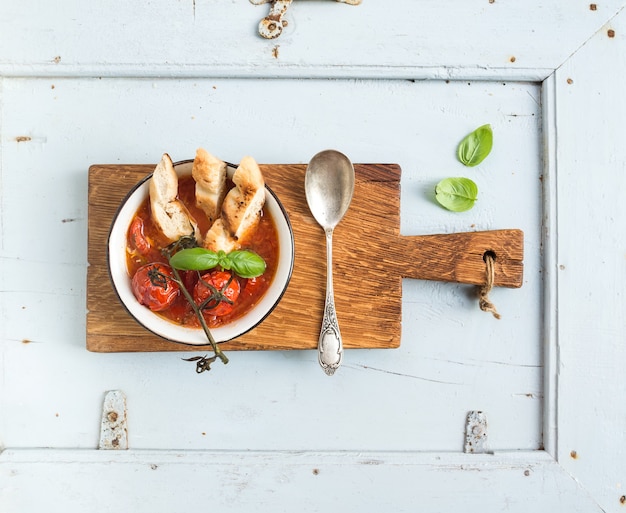 Italiaanse tomaat, knoflook en basilicum soep Pappa al Pomodoro in metalen kom met brood op rustieke houten bord over lichtblauw