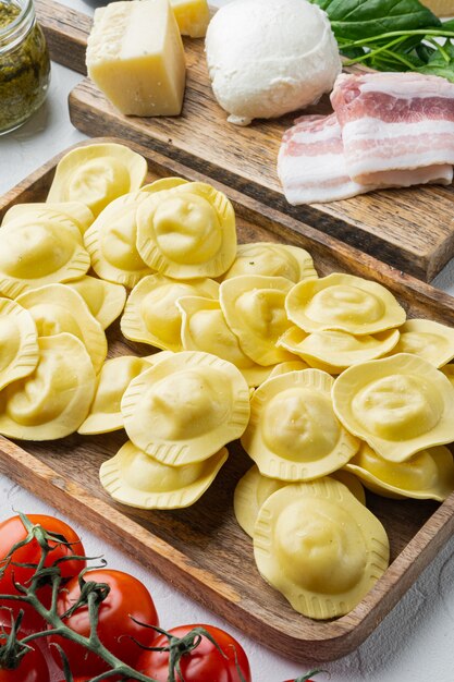 Italiaanse zelfgemaakte ravioli met ingrediënten, ham, basilicum, pesto, mozzarella set, op houten dienblad, op witte tafel