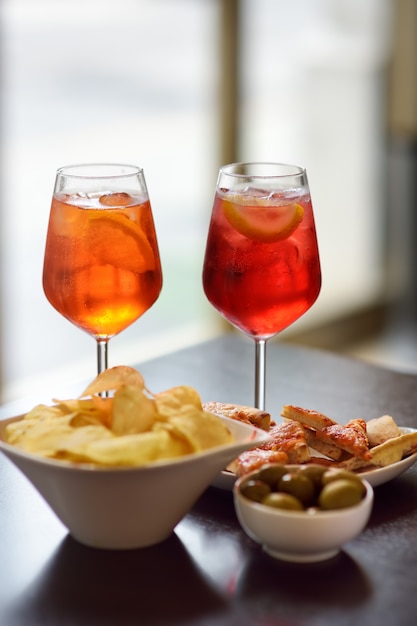 Italian aperitives/aperitif: glass of cocktail (sparkling wine with Aperol) and appetizer platter on the table.