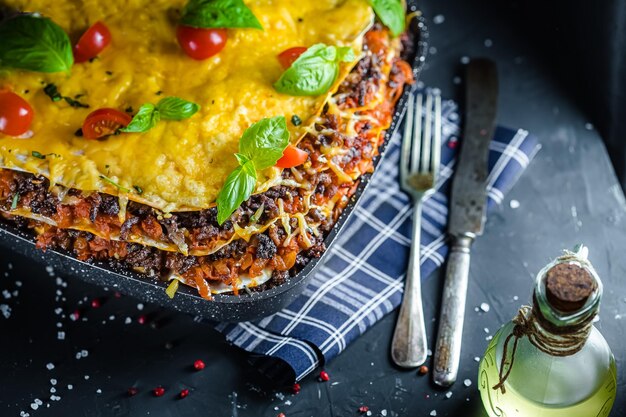 Italian black lasagna in a deep rectangular clay pot or plate or dish or pan, on a black marble