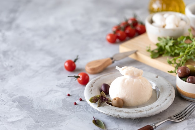 Italian burrata cheese on a round white plate and ingredients for salad