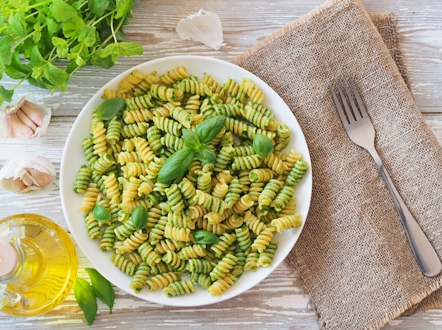 Italian calssic pasta with green pesto on a white plate on a rustic wooden table