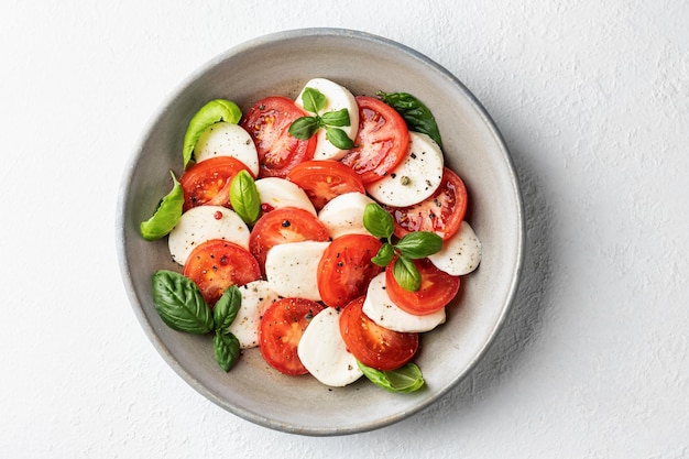 Italian caprese salad with sliced tomatoes mozzarella basil olive oil on white background with copy space Top view