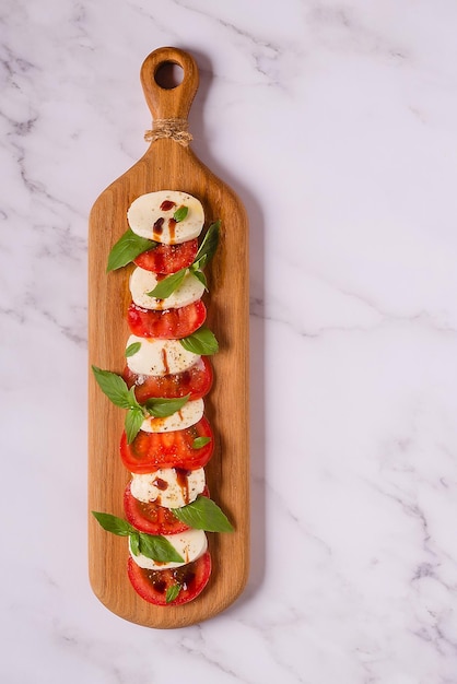 Italian caprese salad with sliced tomatoes, mozzarella, basil, olive oil on a wooden serving board.