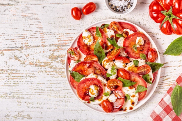 Italian caprese salad with sliced tomatoes, mozzarella cheese, basil, olive oil, balsamic vinegar. Top view, copy space.