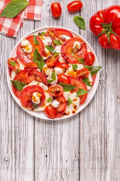 Italian caprese salad with sliced tomatoes, mozzarella cheese, basil, olive oil, balsamic vinegar. Top view, copy space.