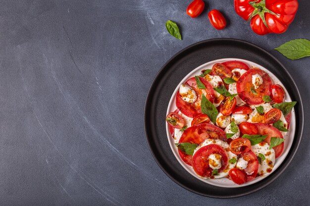 Italian caprese salad with sliced tomatoes, mozzarella cheese, basil, olive oil, balsamic vinegar. Top view, copy space.