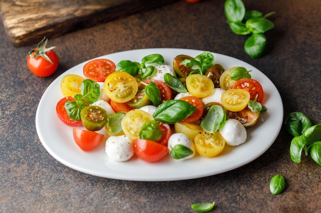 Italian caprese salad with sliced tomatoes, mozzarella cheese, basil, olive oil in wooden bowl. Italian food