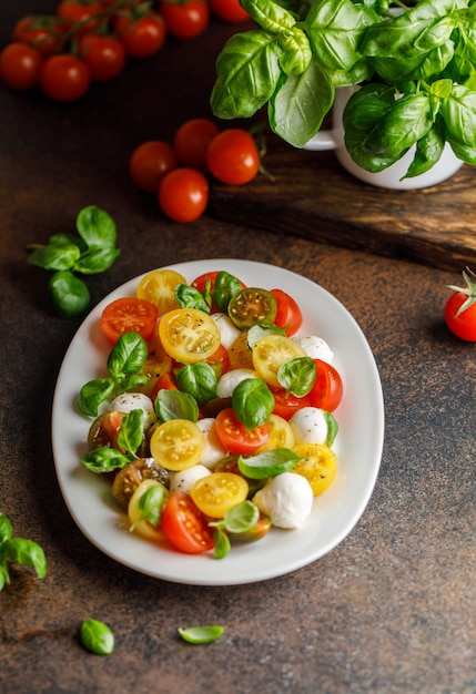 Italian caprese salad with sliced tomatoes, mozzarella cheese, basil, olive oil in wooden bowl.