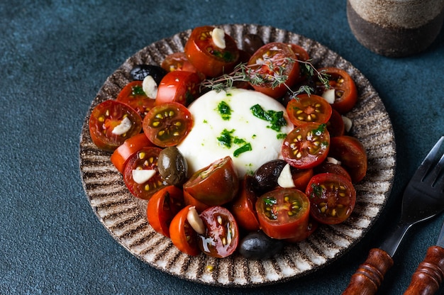 Italian caprese salad with sliced tomatoes, mozzarella cheese, olive oil on dark background. Black tomato salad with burrata and garlic. Comfort food. Sustainable consumption