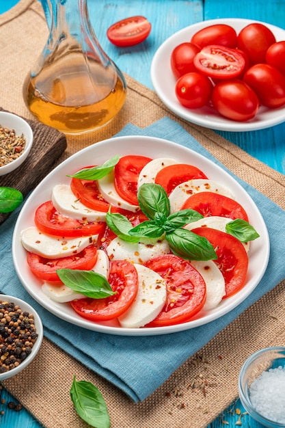 Italian caprese salad with tomatoes, mozzarella and basil on a blue background. Vertical view.