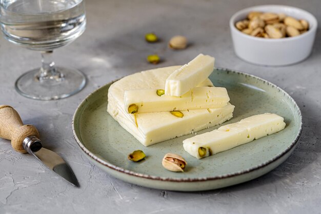 Asiago di formaggio italiano con pistacchi su tagliere nero di pietra con pistacchi di coltello da formaggio in ciotola e tovagliolo verde