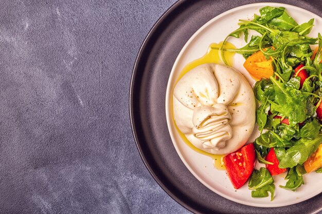 Foto burrata di formaggio italiano con rucola fresca, pomodori, olio d'oliva