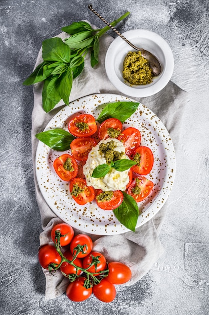 Итальянский сыр stracciatella (буррата) на маленькой тарелке, подается со свежими помидорами и базиликом.