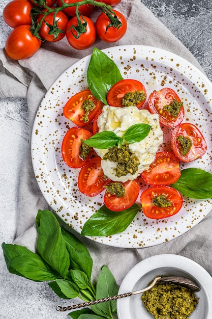 Italian cheese stracciatella on small plate served with fresh tomatoes and basil.