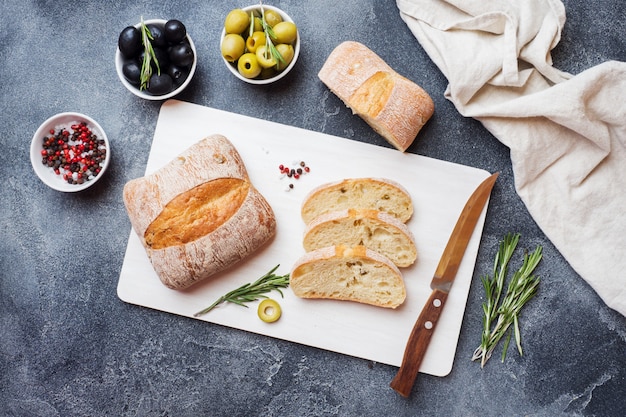 올리브와 커팅 보드에 로즈마리 이탈리아 ciabatta 빵. 어두운 구체적인 배경입니다.