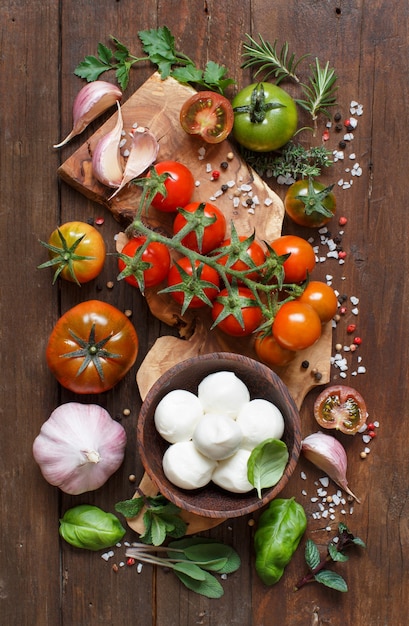 Ingredienti della cucina italiana mozzarella, pomodori, aglio, erbe aromatiche e altro sulla vista dall'alto del tavolo in legno