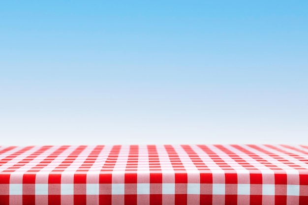 Italian cooking template blank table with a red checked tablecloth on a blue sky background with copy space