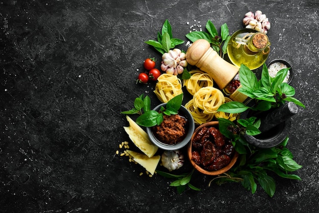 Italian cuisine background pasta basil parmesan pesto tomatoes and nuts olive oil On a black stone background background