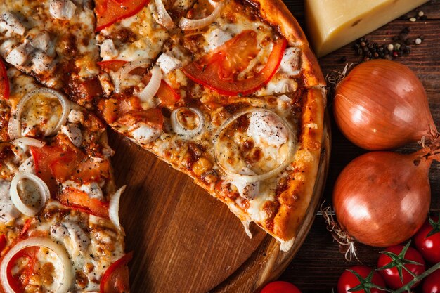 Italian cuisine. Delicious pizza with tomatoes and onion cut slice on wooden table closeup view.