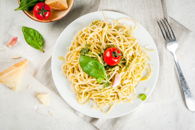 Cucina italiana pranzo o cena per un pesto di pasta spaghetti con pesto foglie di basilico aglio parmigiano e pomodorini una porzione su un tavolo di pietra bianca