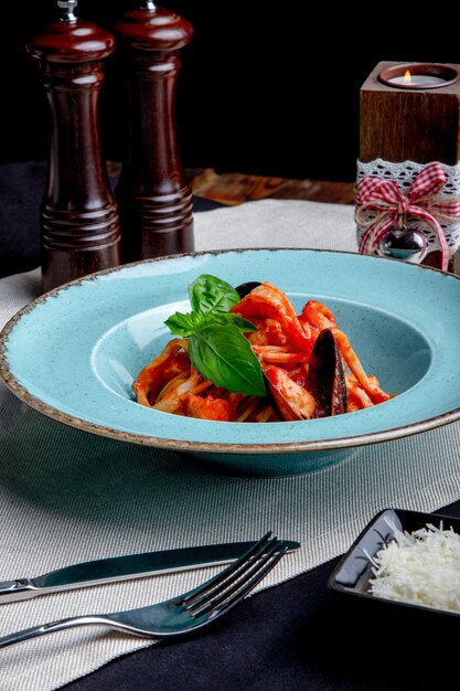 Foto cucina italiana. pasta con frutti di mare, pomodori e formaggio in un blu, una forchetta e un coltello su una luce