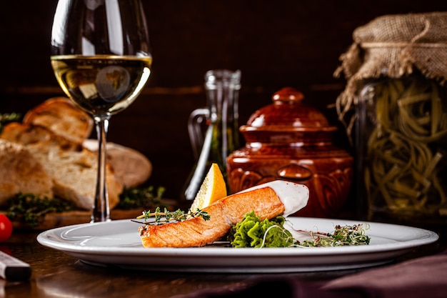 Italian Cuisine. Red fish steak, salmon with lemon, a side dish of spinach. Beautiful restaurant serving in a white plate with a glass of white wine