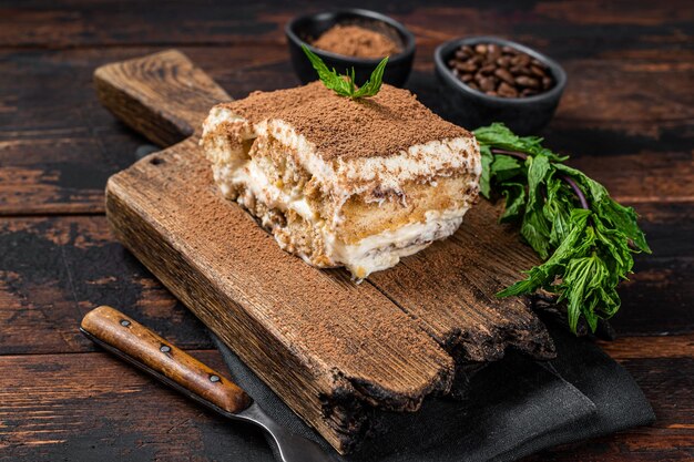 Italian dessert Tiramisu cake with cocoa and mint on a wooden board. Dark Wooden background. Top view.